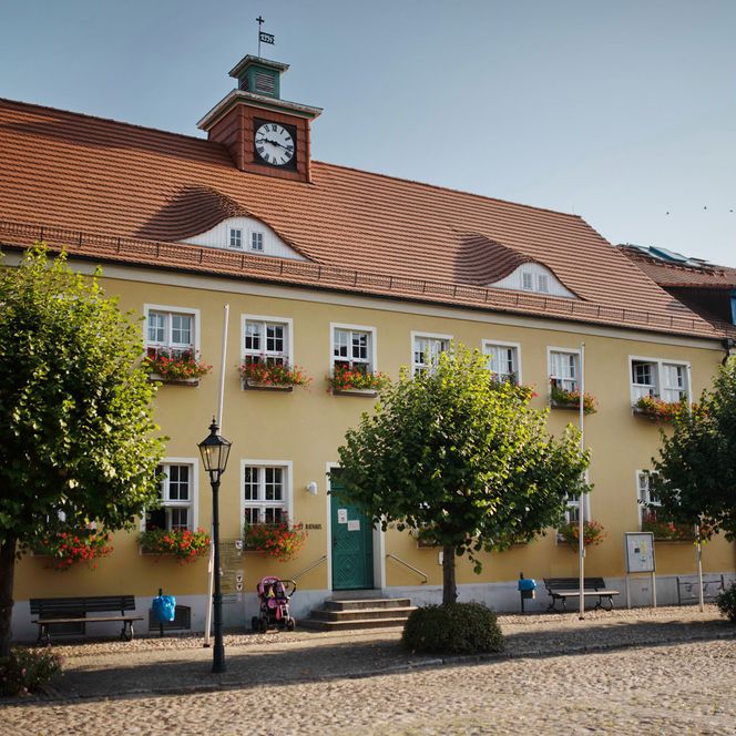Rathaus am Markt in Friesack mit gelber Fassade und roten Blumen an den Fenstern