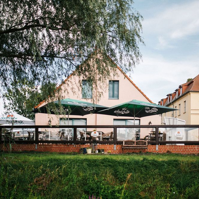 Blick vom Fluss zur Terrasse mit offenen Sonnenschirmen vom Gasthof Milow