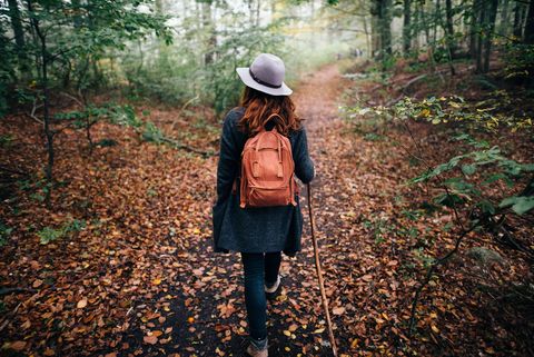 Frau mit Hut und Rucksack wandert durch einen Herbstwald mit Laub am Waldboden