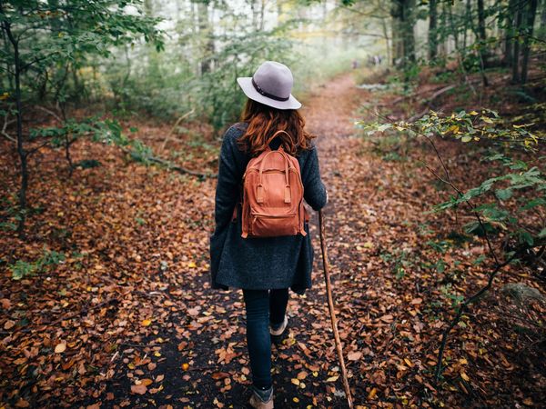 Frau mit Hut und Rucksack wandert durch einen Herbstwald Frau mit Hut und Rucksack wandert durch einen Herbstwald mit Laub am Waldboden
